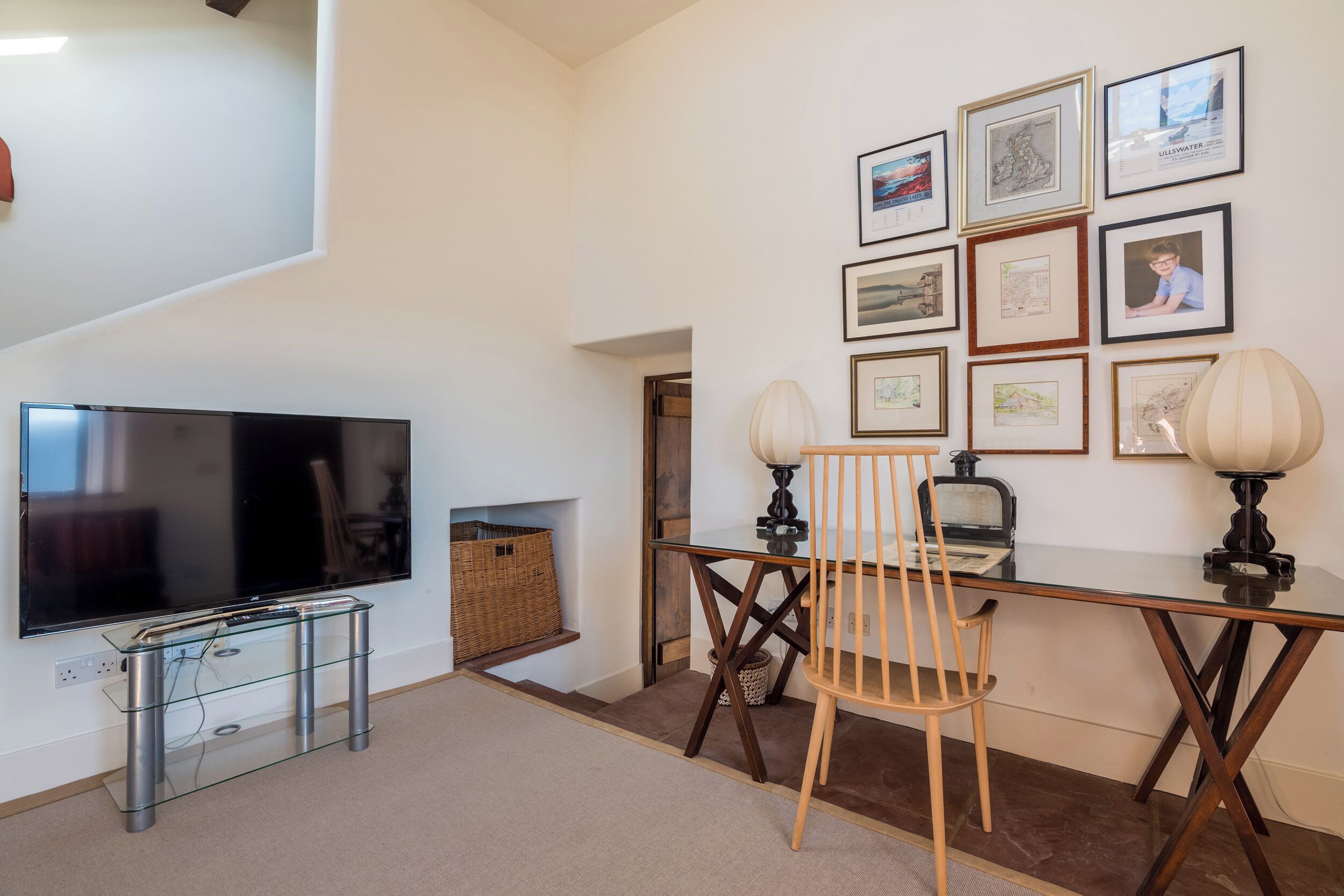 A living room with a flat-screen TV, a glass coffee table, a wooden chair, and a wall adorned with framed pictures.