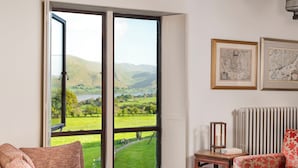 Une pièce dotée d’une grande fenêtre donnant sur un paysage verdoyant et des montagnes. On y trouve deux cartes encadrées accrochées au mur, un radiateur et une petite table sur laquelle est posée une bougie.