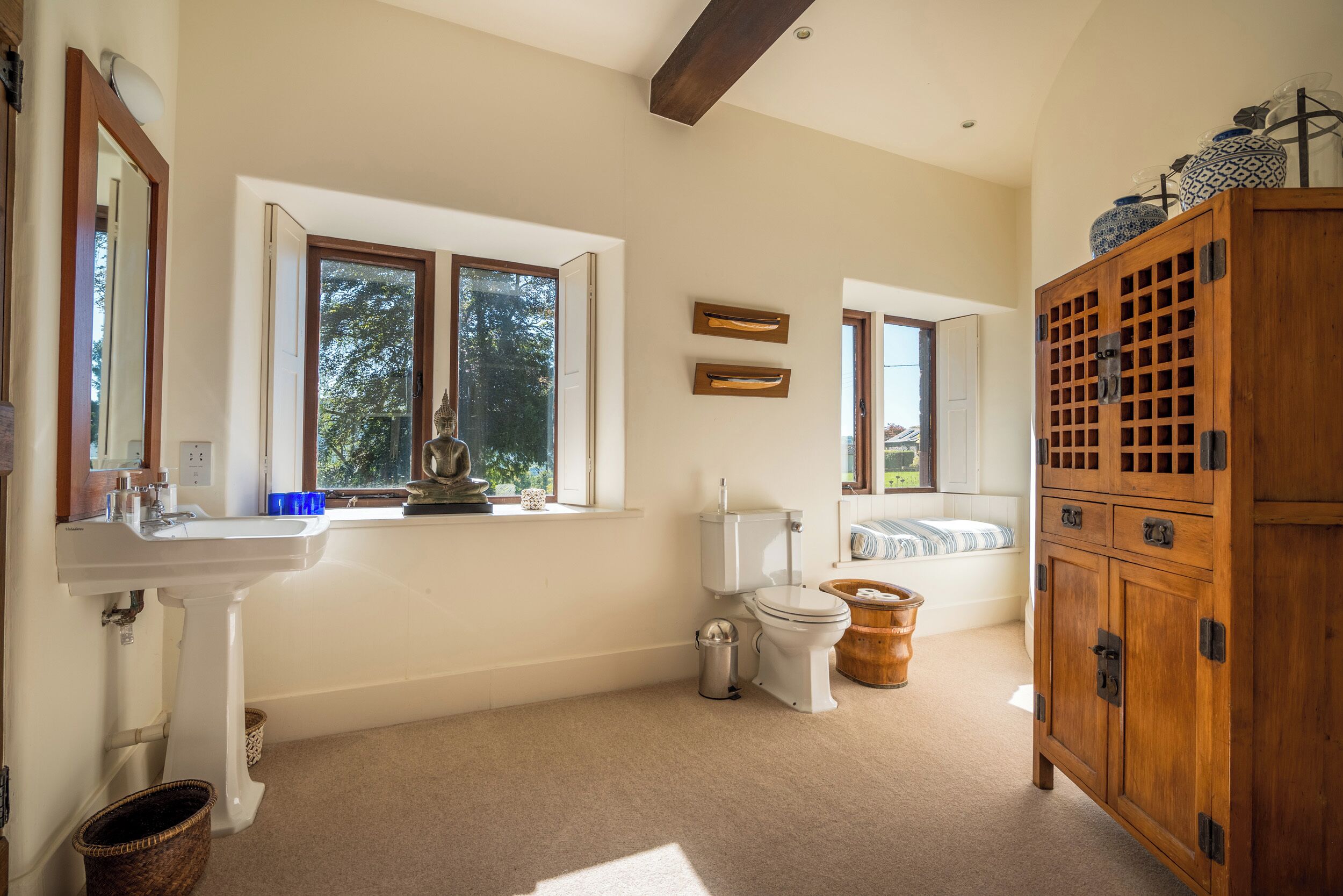 Un baño con lavamanos, inodoro y ventana. Hay un armario de madera y una cesta en el suelo.