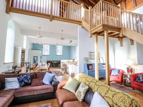 Un vaste espace de vie doté d’un haut plafond, d’un escalier en bois et d’un coin repas avec une table de billard.