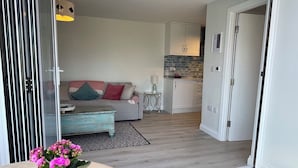 Una sala de estar moderna con un sofá gris, una mesita y una cocina al fondo.