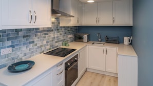 Una cocina moderna con armarios blancos, un salpicadero de azulejos azules, horno empotrado y tostadora.