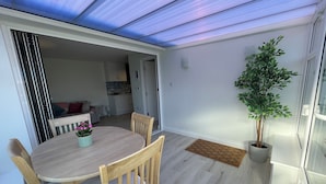 Un comedor con una mesa y sillas, una planta en maceta, y vistas a una cocina y un espacio de sala a través de una puerta abierta.