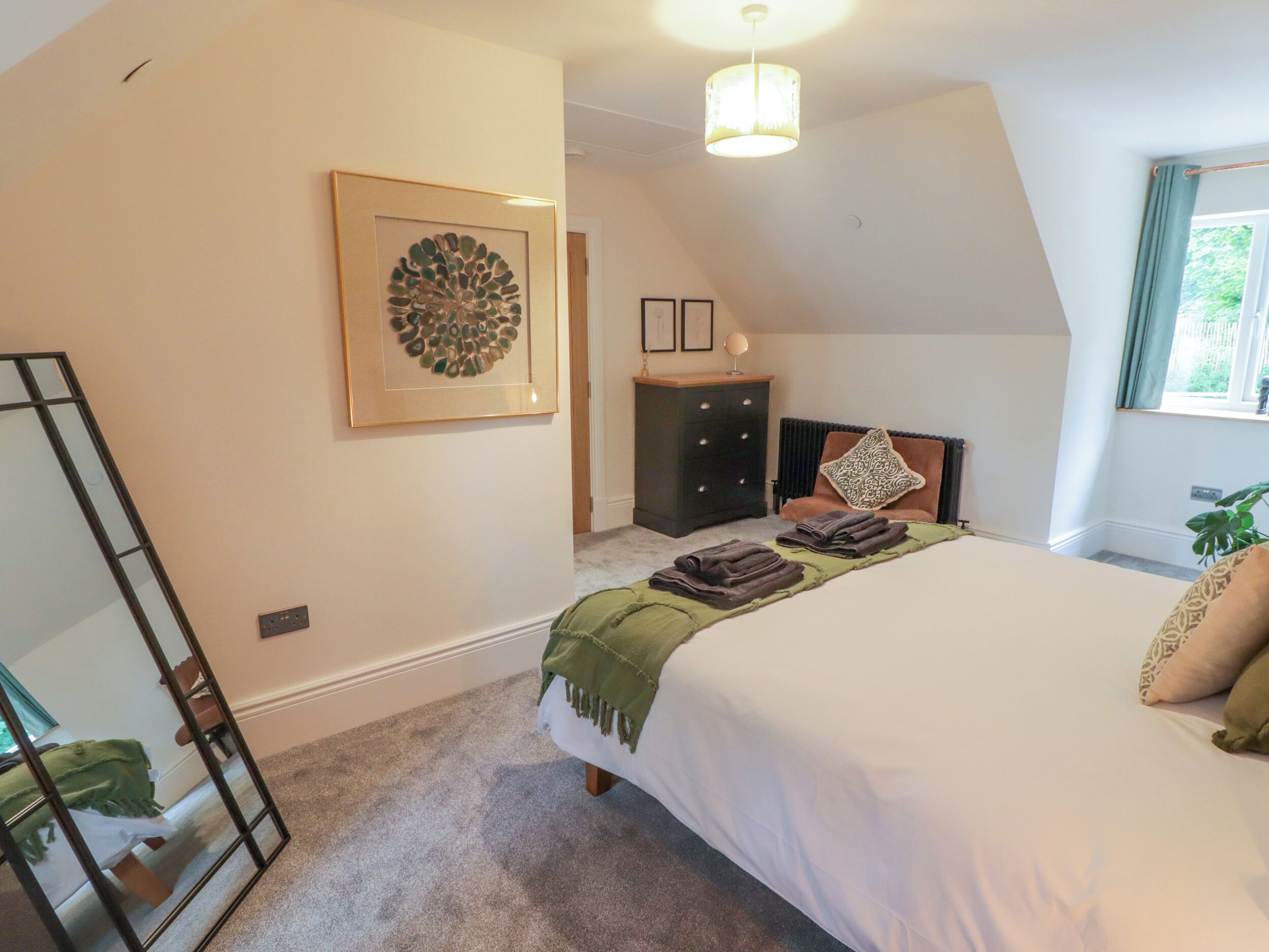 A bedroom with a bed, a dresser, a mirror, a framed artwork, and a window with curtains.