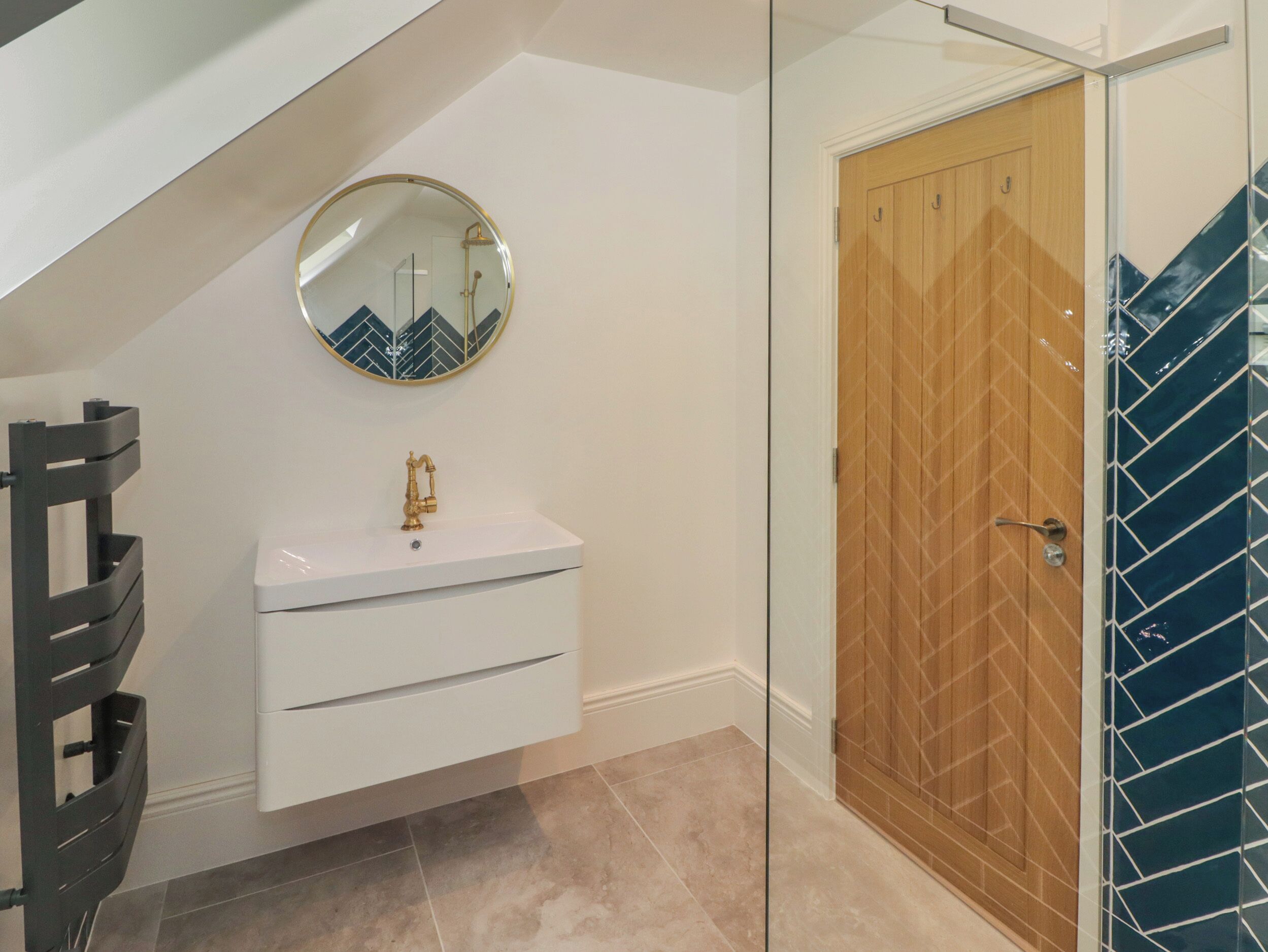 A bathroom with a white vanity, a round mirror, a shower, and a wooden door.