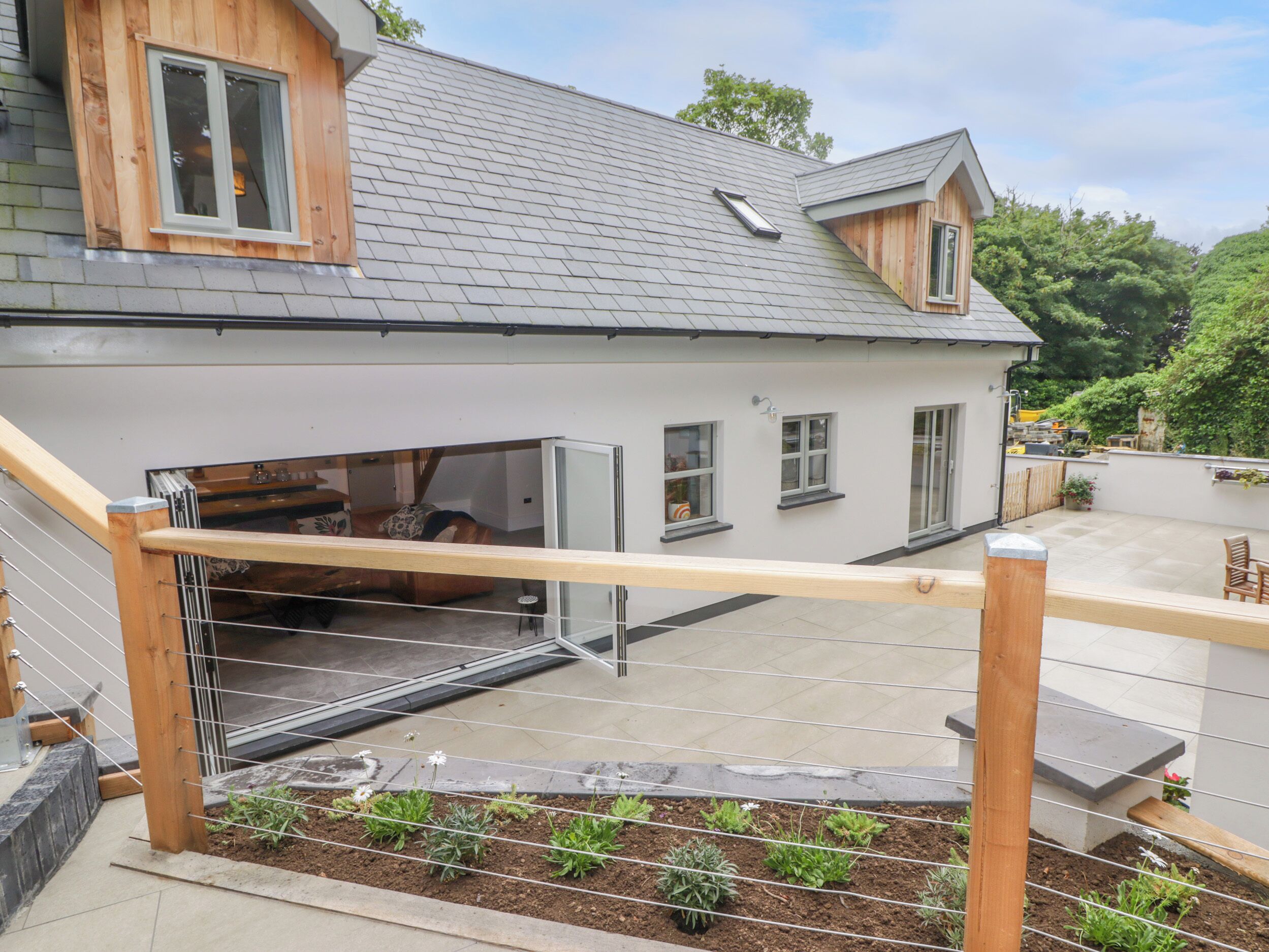 Una casa moderna con terraza de madera, puerta de cristal y un pequeño jardín.