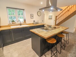 Una cocina moderna con una isla central, muebles oscuros, una ventana con vistas y una escalera que sube a otro nivel.