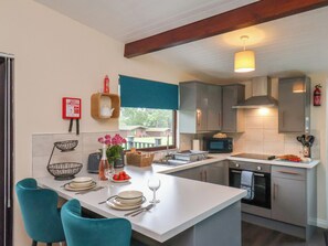 Cocina moderna con isla central, microondas y estufa. Hay sillas color turquesa y una mesa de comedor para dos personas.