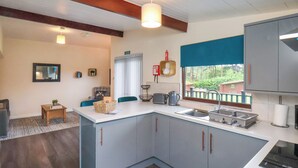 A compact kitchen with a central island, a dining area with a table and chairs, and a view of the outdoors through a window. - Ramson (Saltburn-by-the-Sea)