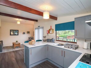 A compact kitchen with a central island, a dining area with a table and chairs, and a view of the outdoors through a window. - Ramson (Saltburn-by-the-Sea)