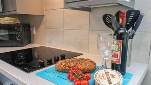 Una encimera de cocina con una hogaza de pan, una botella de vino, una copa y una tabla de cortar con tomates.