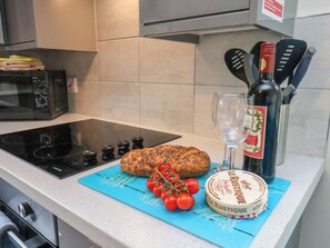 A kitchen counter with a loaf of bread, a bottle of wine, a glass, and a cutting board with tomatoes. - Ramson (Saltburn-by-the-Sea)