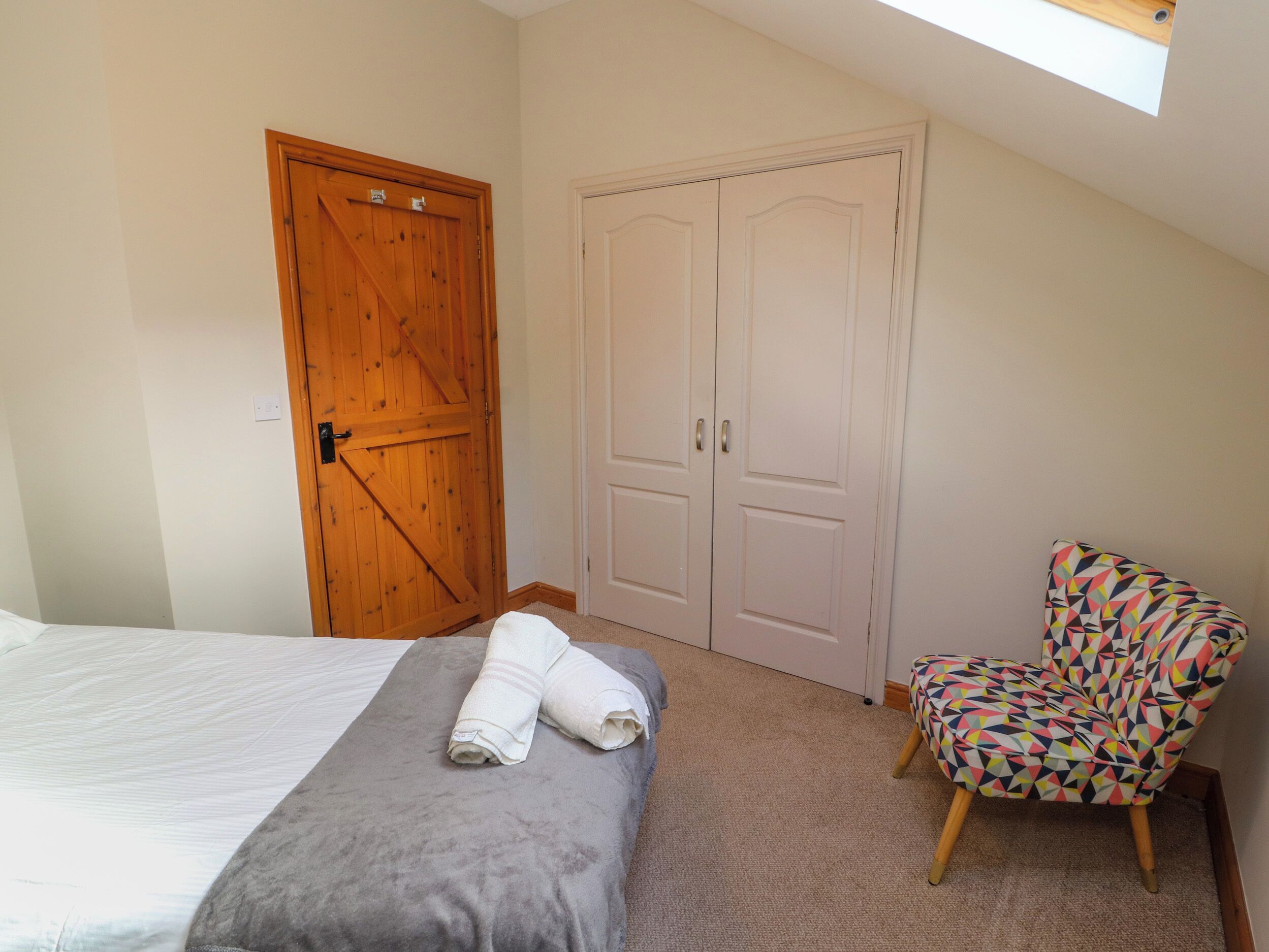 Un dormitorio con cama, una puerta de madera, un armario blanco y una silla colorida.