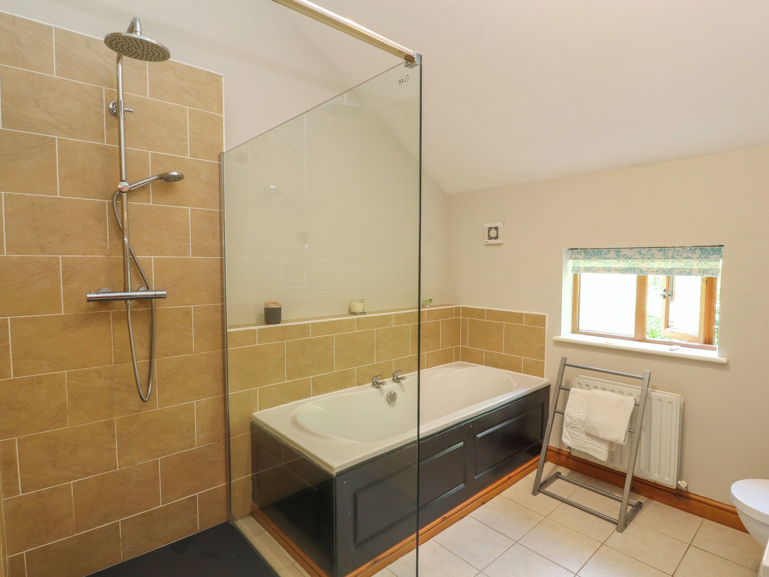 A bathroom with a glass-enclosed shower, a bathtub, and a window with a curtain.