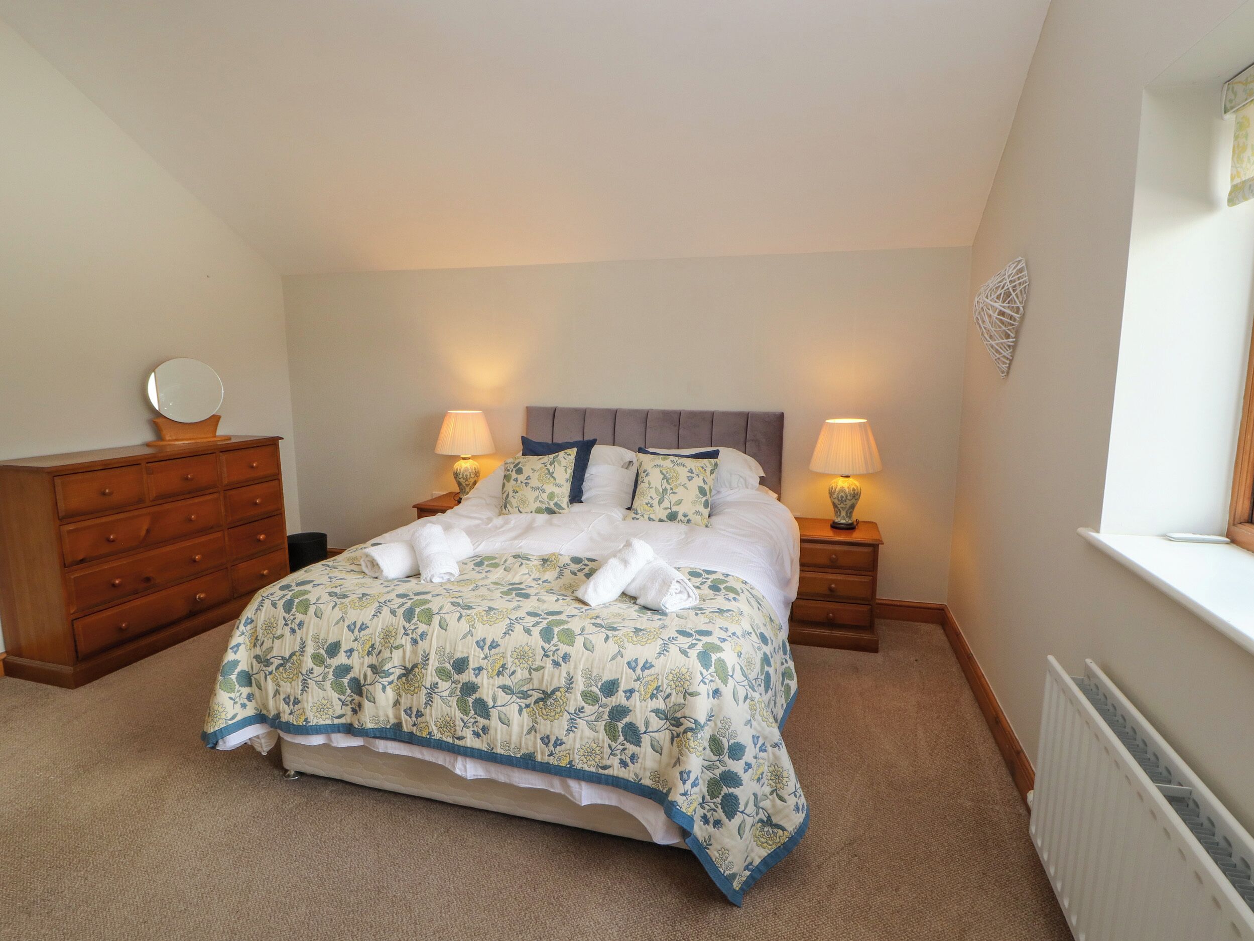 A bedroom with a bed, two bedside tables with lamps, a dresser, and a radiator.