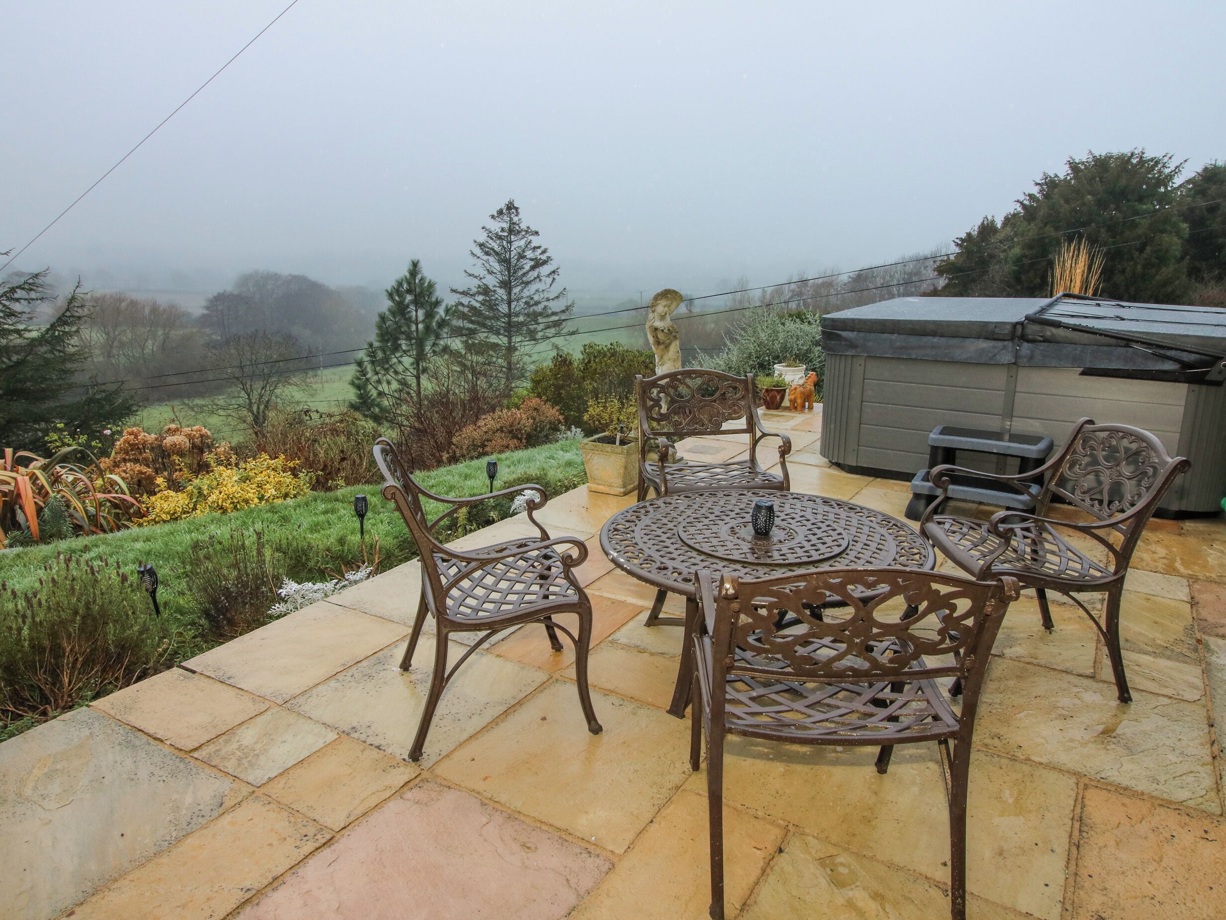 Une terrasse avec une table ronde et quatre chaises, une petite statue et un jacuzzi.