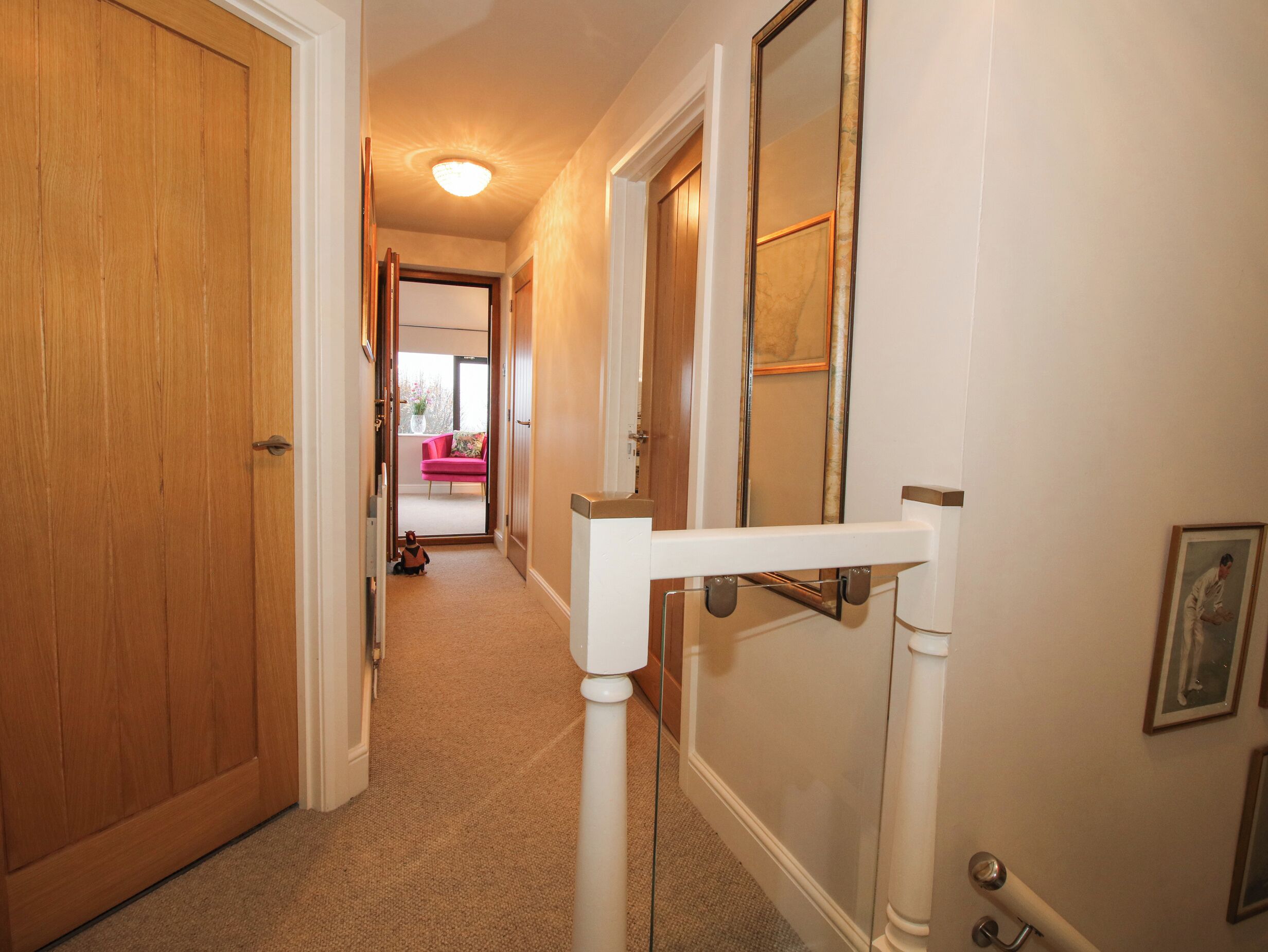 A hallway with a wooden door, a white railing, and a mirror on the wall.