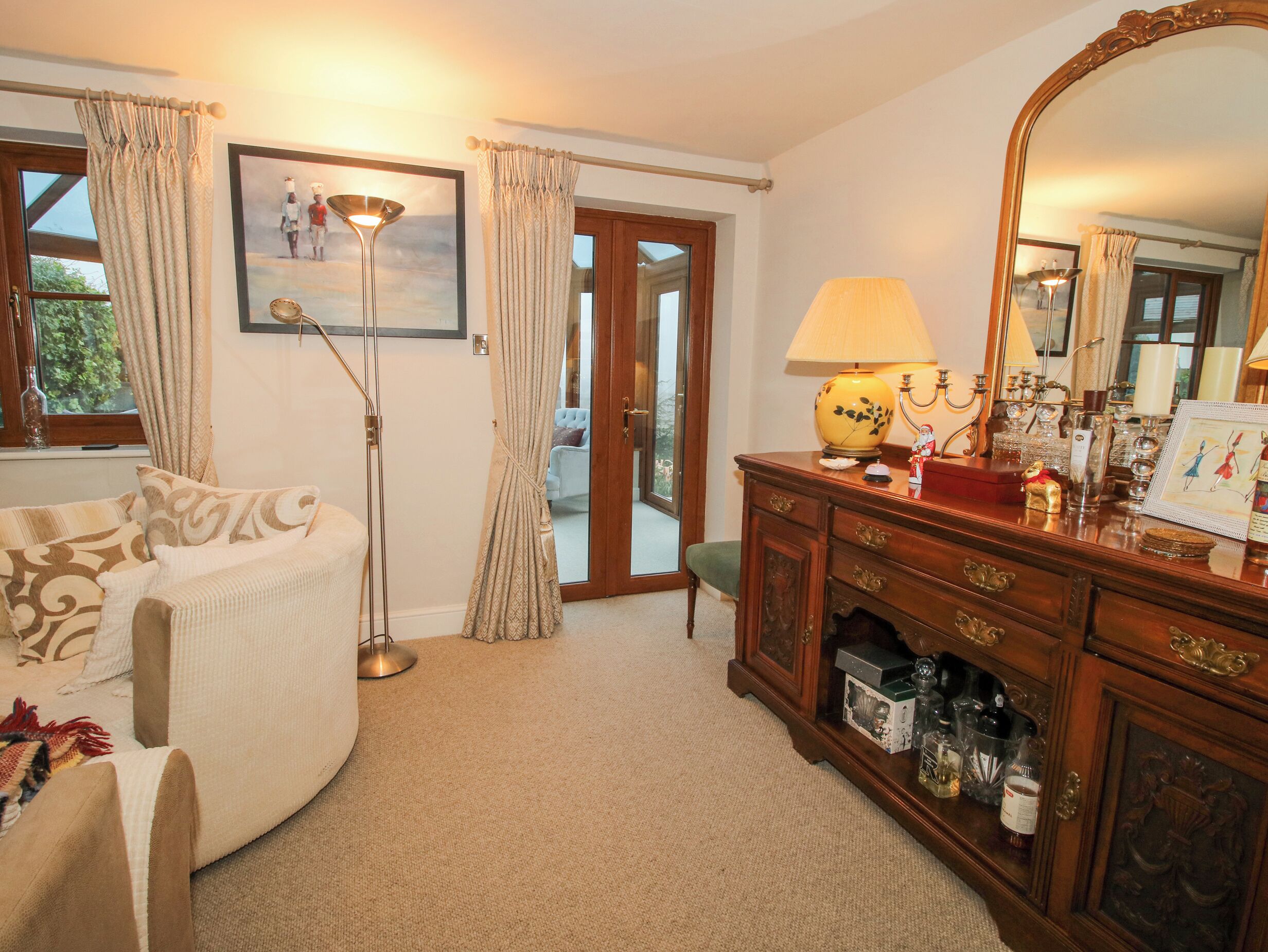 A cozy room with a sofa, a wooden cabinet, a floor lamp, and a large mirror.