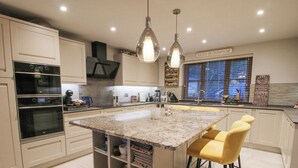 A modern kitchen with a central island, bar stools, built-in ovens, and pendant lighting. - Quarry House (Montgomery)