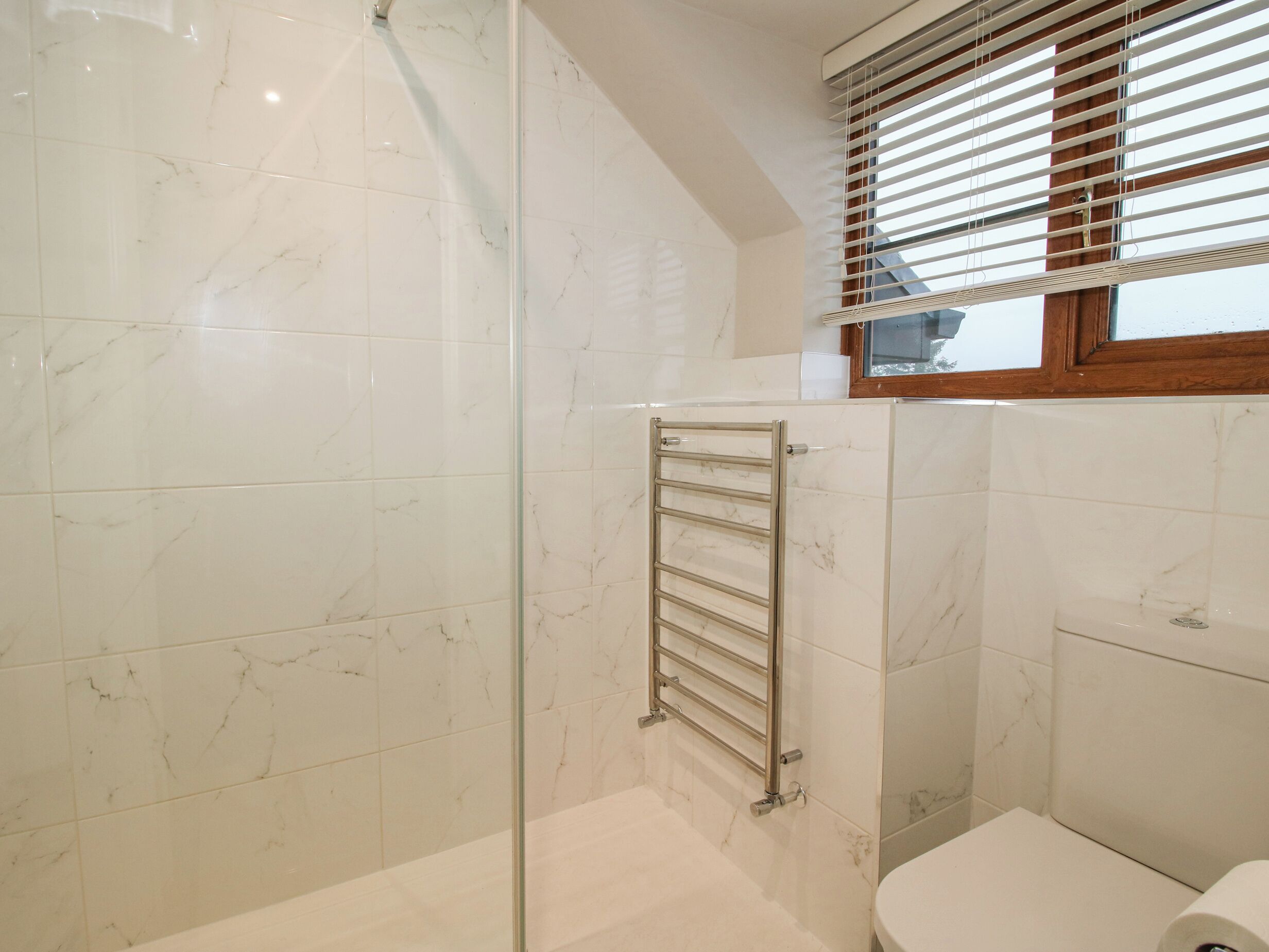 A bathroom with a glass shower enclosure, a towel rack, and a toilet.