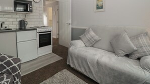 A compact living space with a kitchenette, a sofa, and a painting on the wall. - Flat 4, Big Tree Holiday Flats (Paignton)