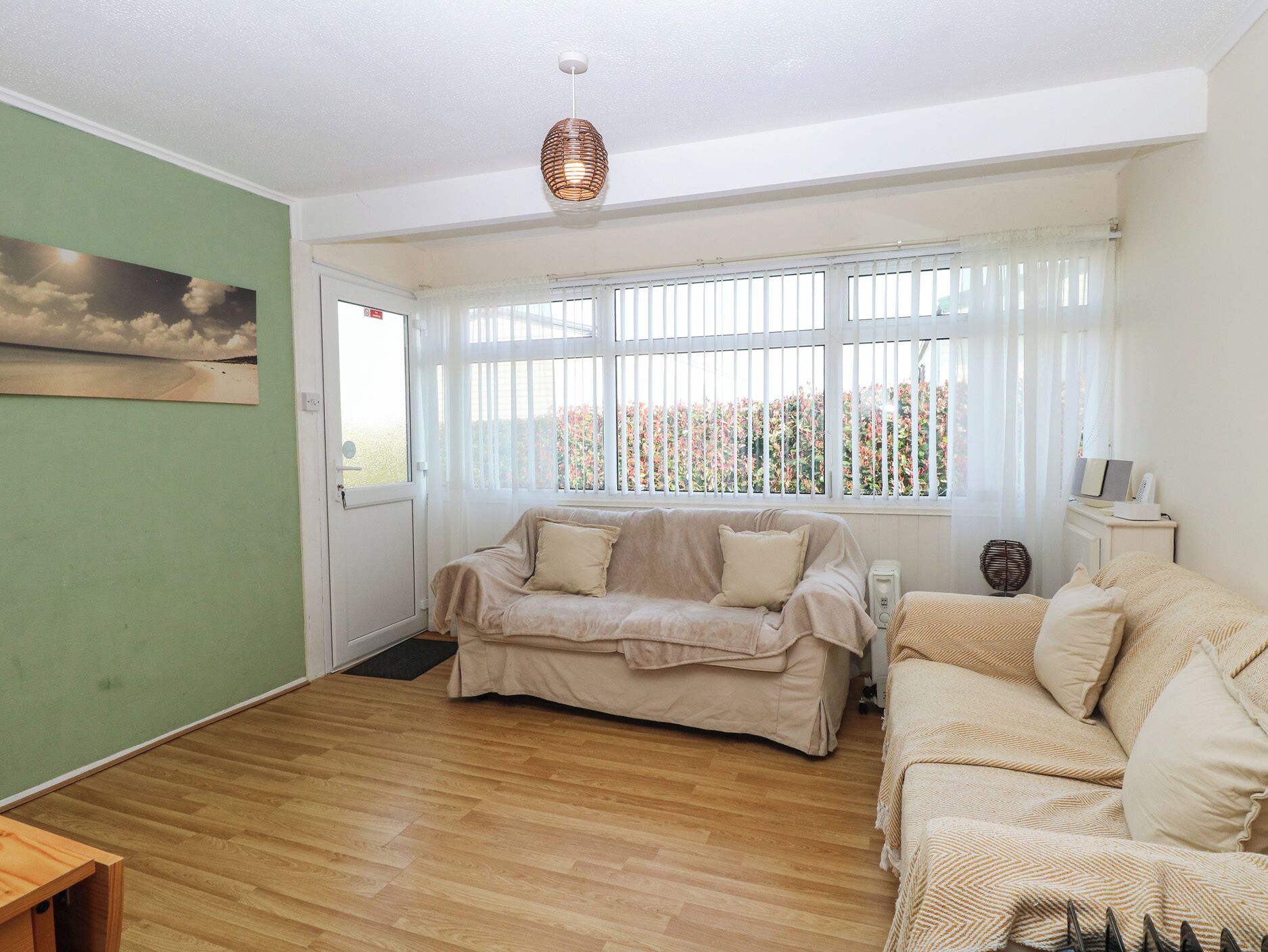 Ein Wohnzimmer mit beiger Couch, Holzboden, einem Fenster mit weißen Jalousien und einem Gemälde an der Wand.