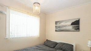 Una camera da letto con un letto, un comodino, una lampada, una finestra con tende e un quadro appeso al muro.