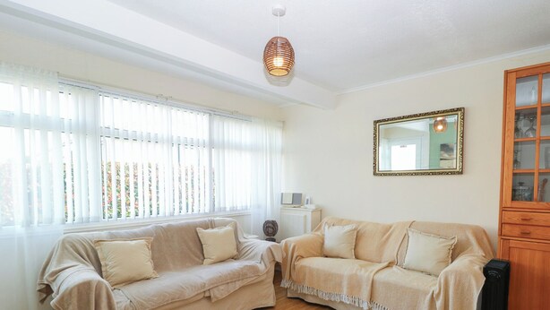 A living room with two beige sofas, a wooden cabinet, and a large window with blinds. - Chalet 469 (Great Yarmouth)