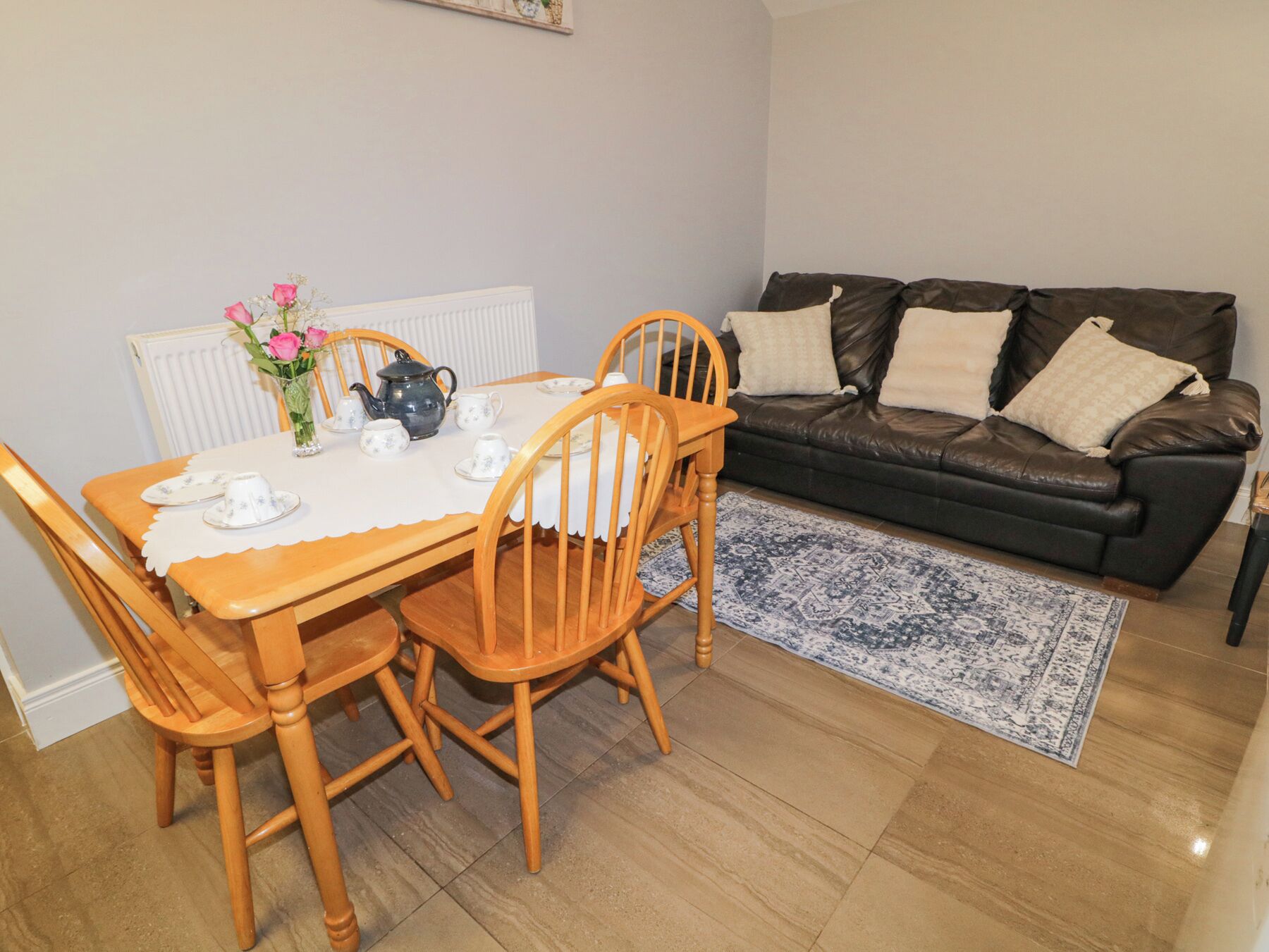 A dining area with a table set for four, a black leather sofa, and a patterned rug.
