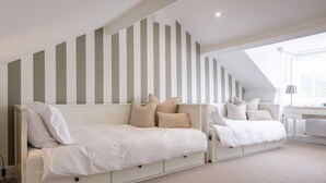 Ein Schlafzimmer mit schrägen Wänden, einem weißen Bett mit vielen Kissen, einem weißen Schreibtisch und einer Heizung.
