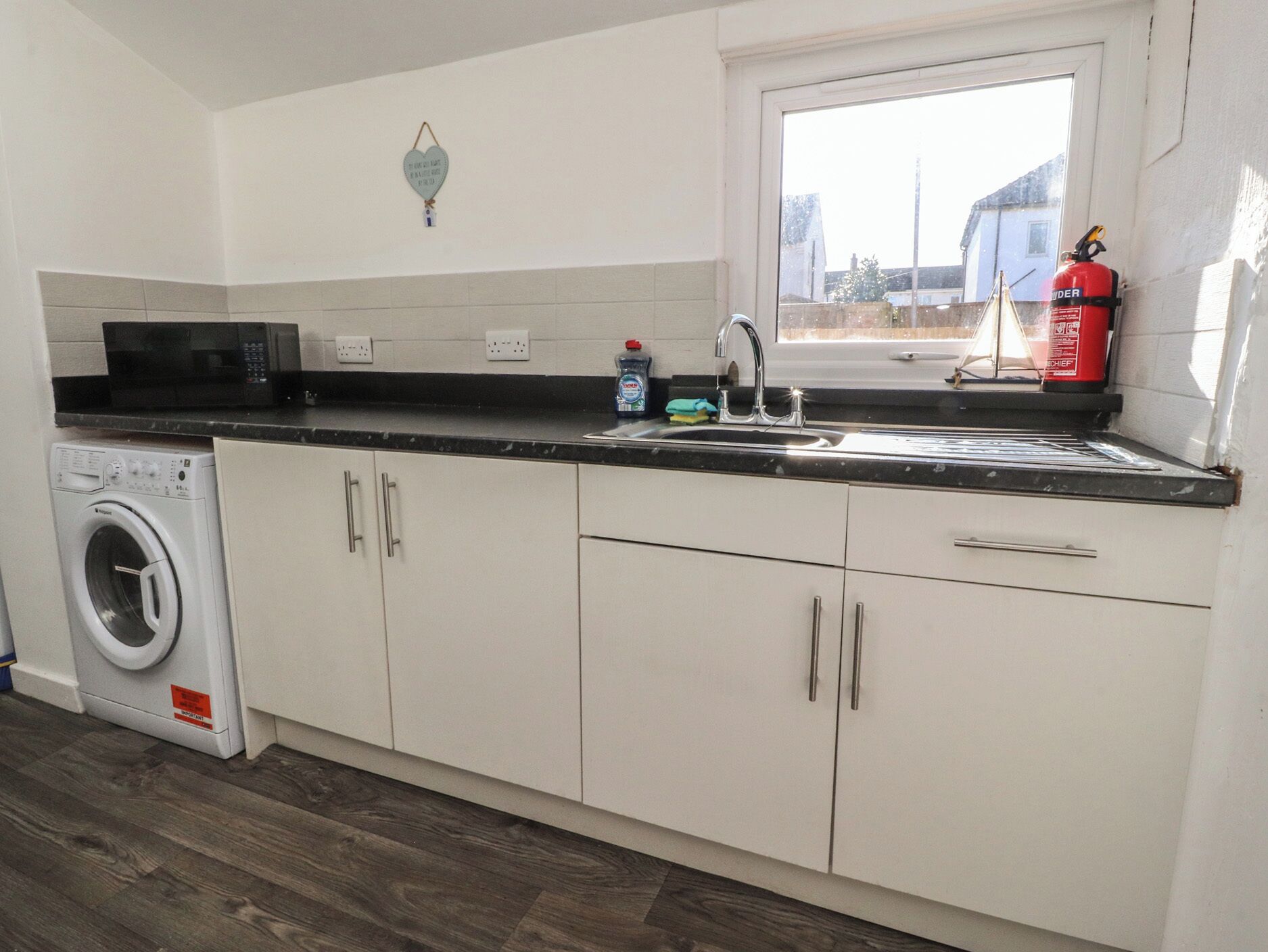 A kitchen with a washing machine, a microwave, a sink, and a fire extinguisher.