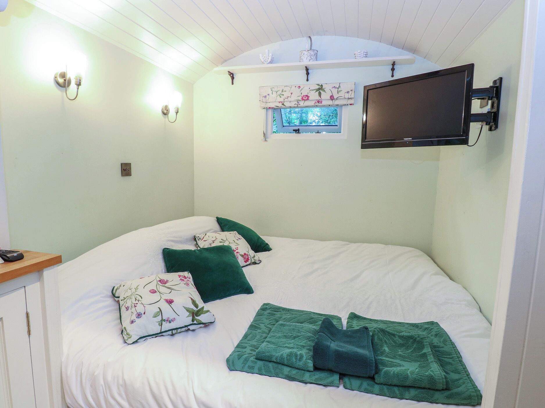 A bedroom with a bed, pillows, a TV, and a window.