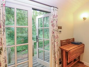 A room with a wooden bench, a table, and a set of double doors leading to a garden.