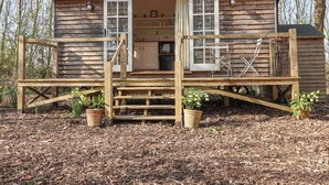 A wooden cabin with a deck, a door, and a window. - Woodlands Retreat Shepherd's Hut (Woodbridge)