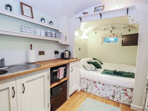 Een kleine keuken met een spoelbak, fornuis en oven. Er is een bed met bloemenbeddengoed en een televisie erboven bevestigd.