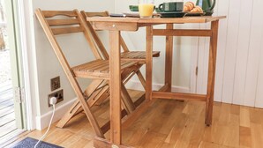 A wooden dining table with a chair, a glass of orange juice, a cup, and a green teapot on the table. - Woodlands Retreat Shepherd's Hut (Woodbridge)