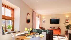 A cozy living room with a dining area, a television, and a window with blinds. - Claire's Cottage (Bangor)