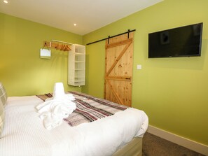 A bedroom with a bed, a TV mounted on the wall, a wooden door, and a white towel on the bed. - Claire's Cottage (Bangor)