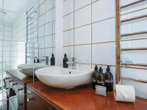 A modern bathroom with a large white sink, a mirror, and a wooden vanity. - Claire's Cottage (Bangor)