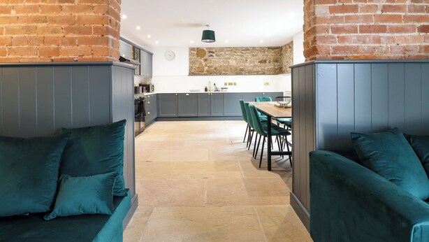 Una cucina moderna con mobili grigi, una parete decorata con pietra e un'area da pranzo con sedie color acquamarina.