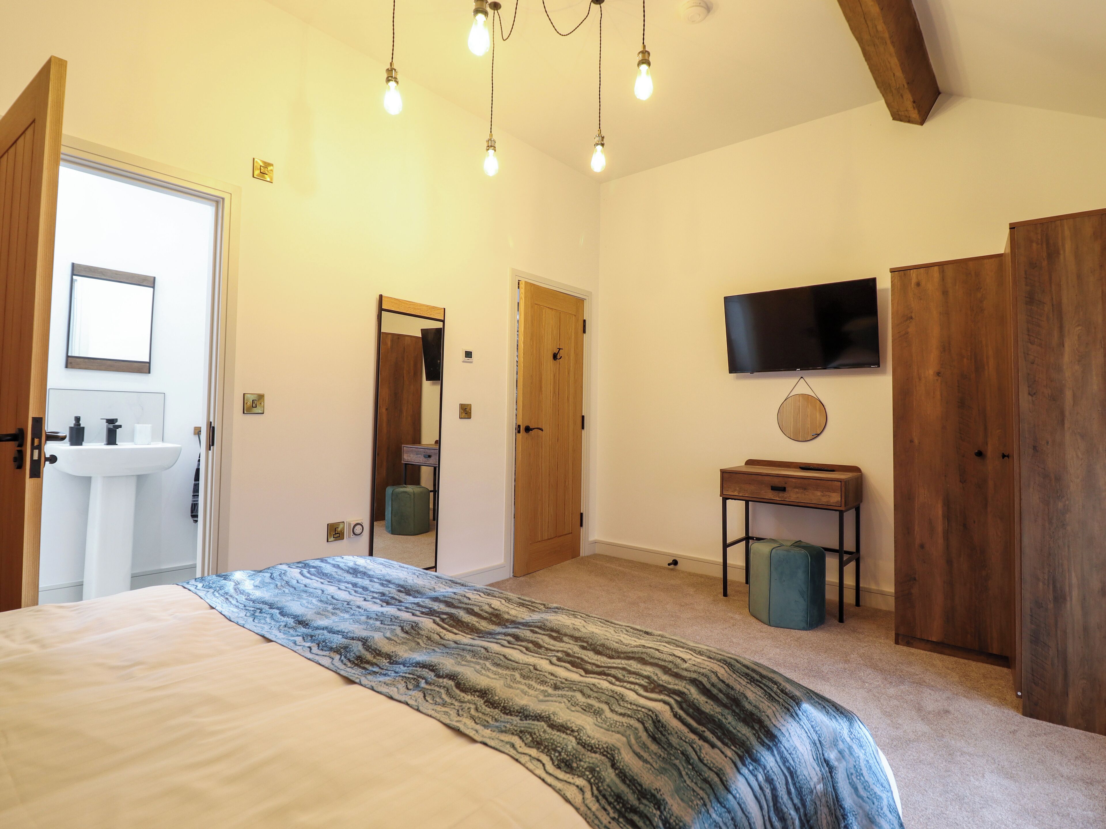 A bedroom with a bed, a wooden wardrobe, a television mounted on the wall, and a small bedside table.