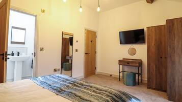 A bedroom with a bed, a wooden wardrobe, a television mounted on the wall, and a small bedside table.