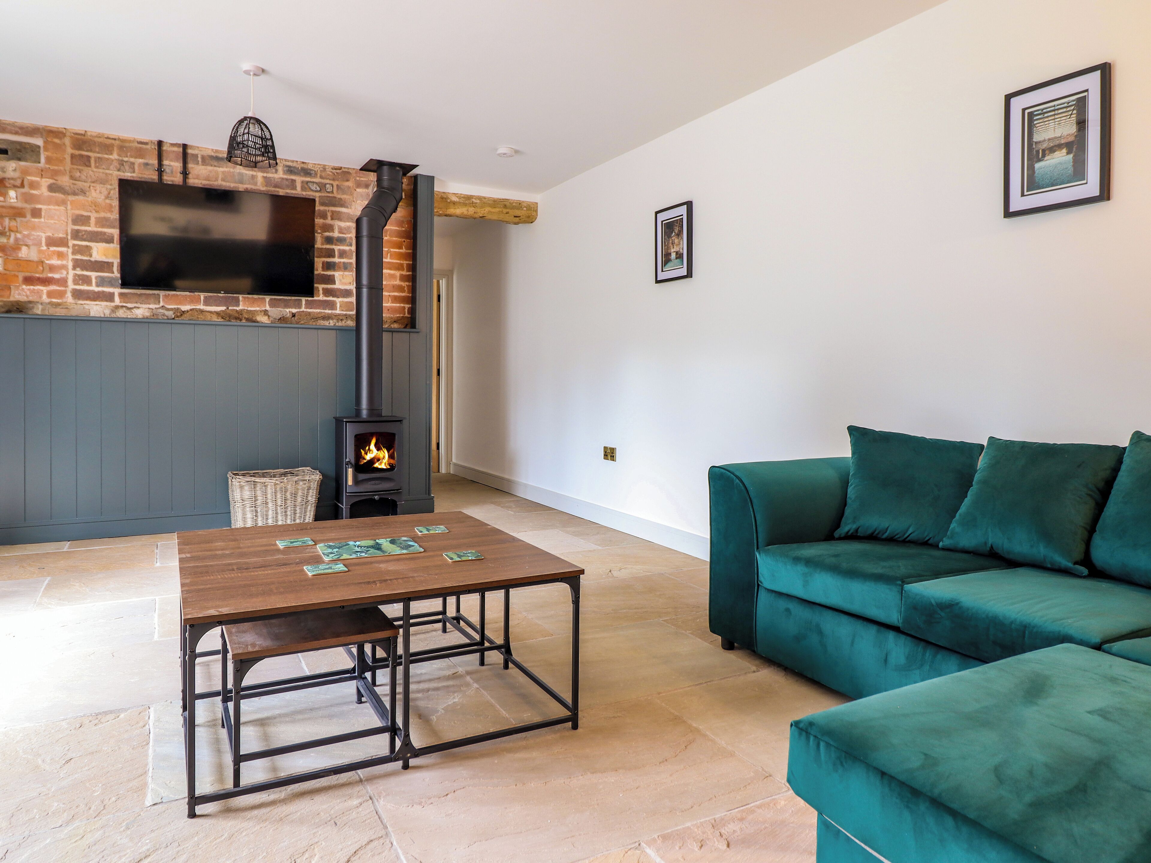 Un salón con chimenea, un sofá verde, una mesa de centro de madera y un televisor instalado en una pared de ladrillo.
