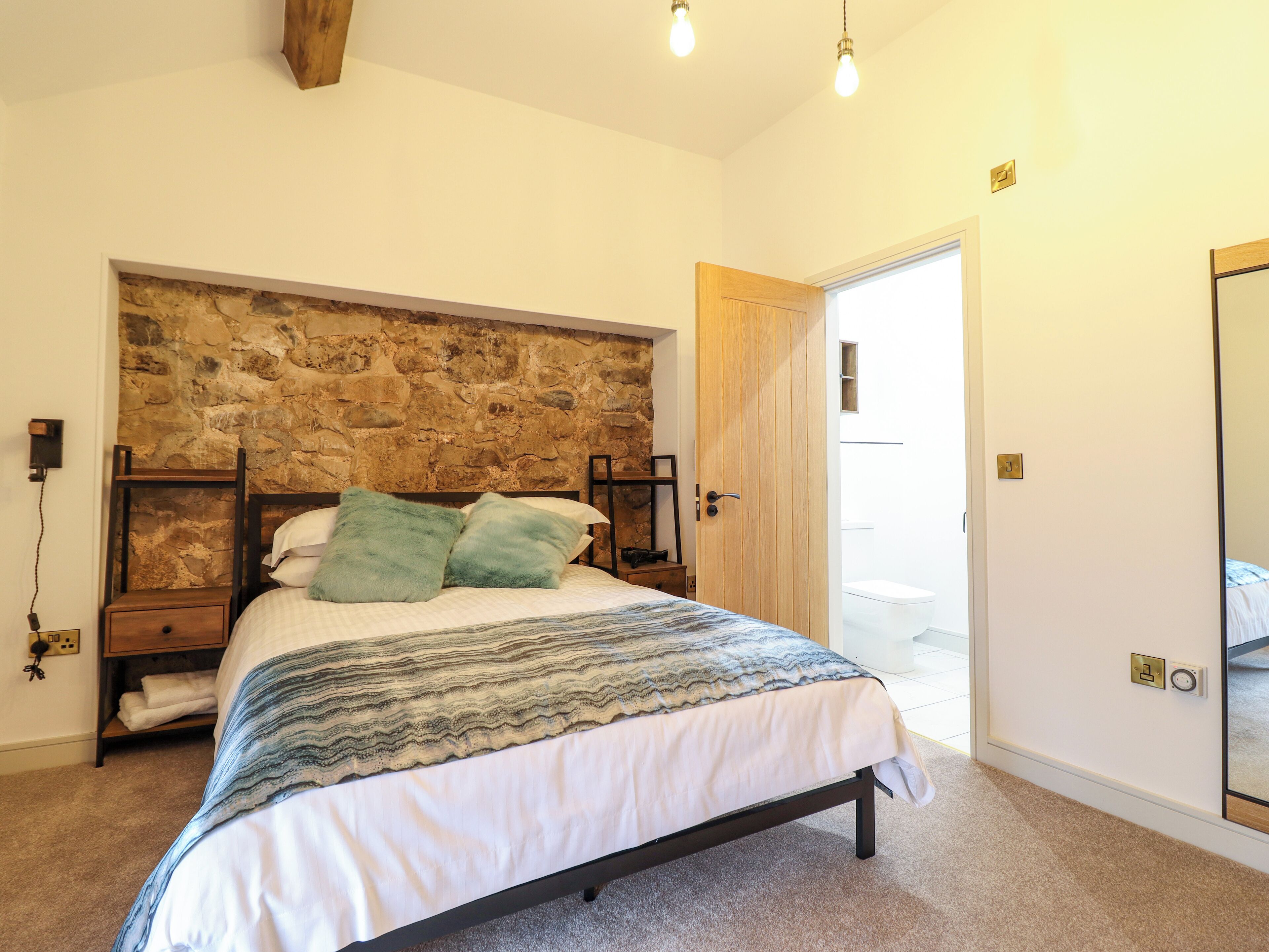 A bedroom with a stone headboard, a bed with a patterned bedspread, a nightstand, and a wooden door.