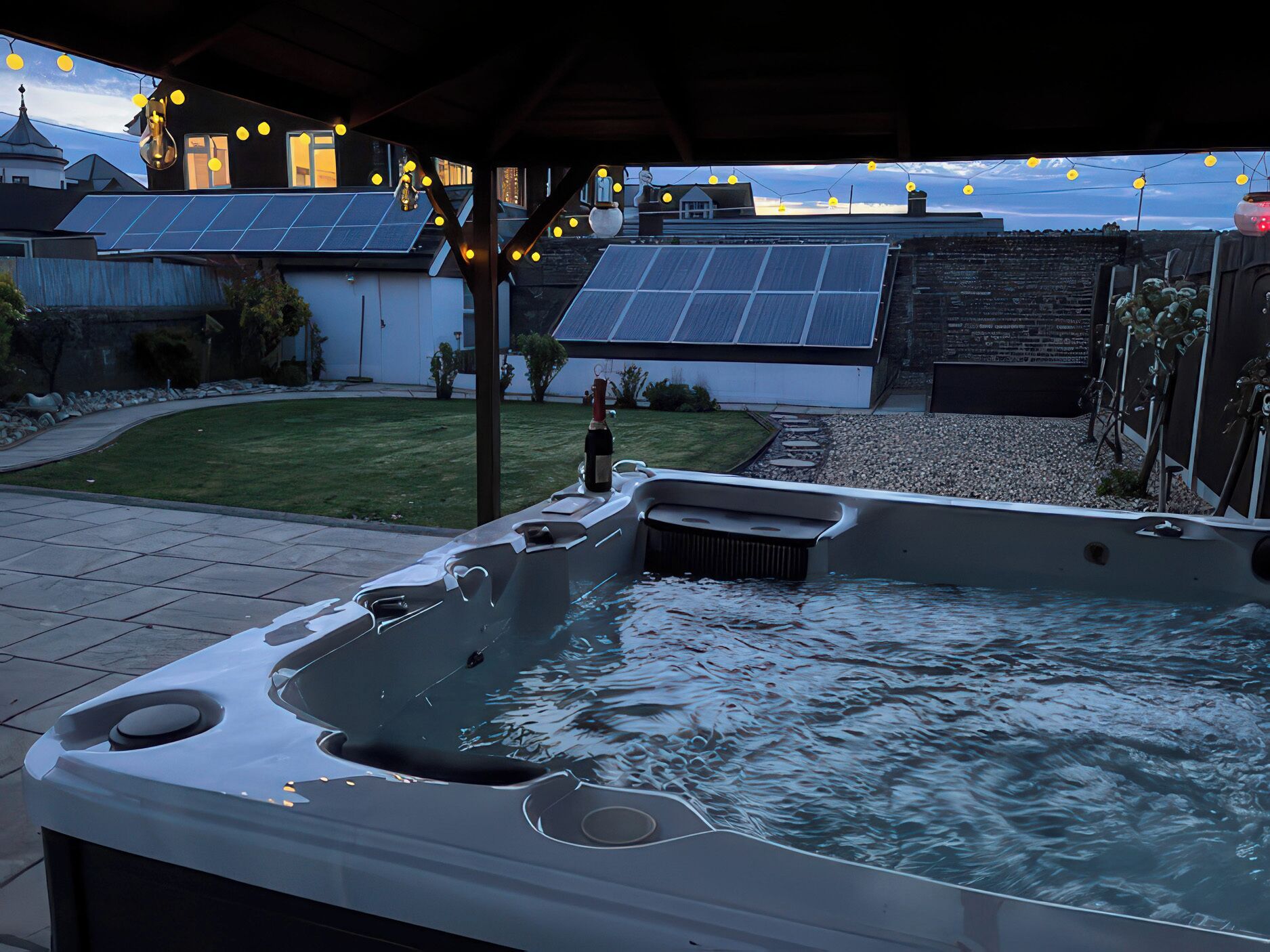 Un jacuzzi con zona de patio, paneles solares y un pequeño jardín.