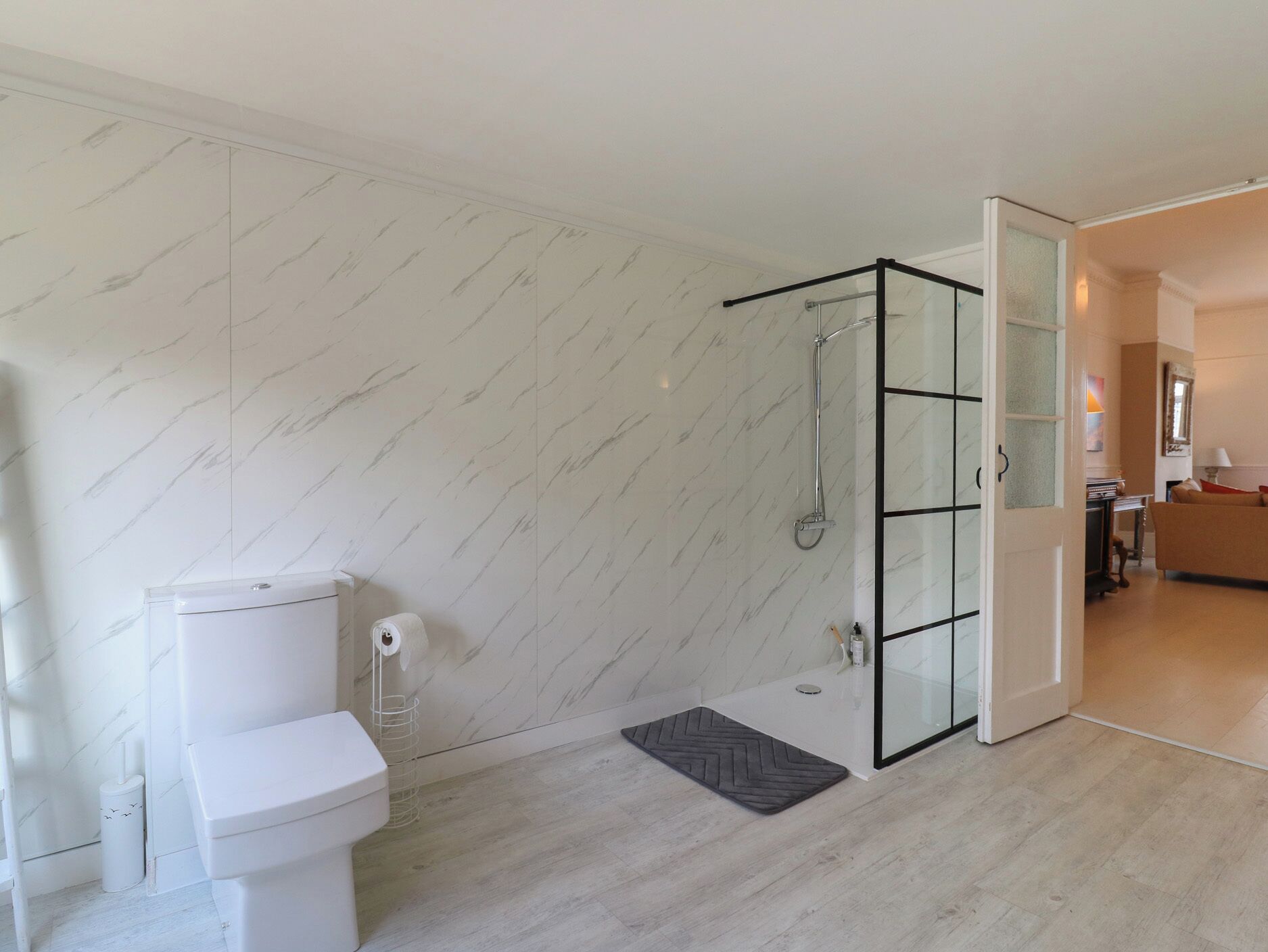 A modern bathroom with a toilet, shower, and glass door leading to a living area.