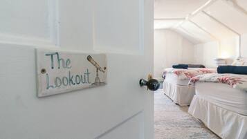 Une chambre avec deux lits, une porte blanche sur laquelle est apposée une pancarte indiquant « Le point de vue », et une illustration représentant un télescope.