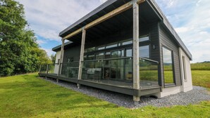 A modern house with a glass balcony, a wooden deck, and a view of the surrounding landscape. - 6 Strathtay Lodges (Aberfeldy)