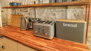 Een keukentafel met een broodrooster, een broodtrommel, een waterkoker en bakken met thee, suiker, koffie en koekjes.