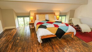 Een slaapkamer met een houten vloer, een bed met een kleurrijk quilt, nachtlampjes, een stoel en uitzicht door een raam.